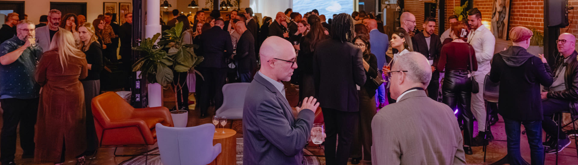 Participants gathered at a networking activity in an event space; several people are conversing in small groups within a setting furnished with armchairs, tables, and plants.