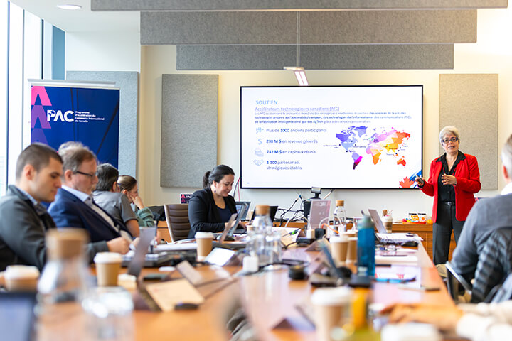 Trade Accelerator Program presentation in a meeting room; participants attend a conference while a speaker presents international market data on a screen.