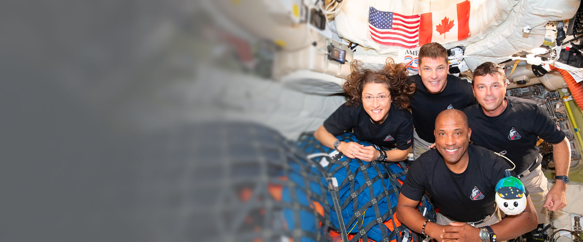 Équipage flottant à l’intérieur d’un module de station spatiale dans le cadre du programme Artemis; on voit du matériel arrimé, des systèmes embarqués et des drapeaux du Canada et des États-Unis, illustrant la collaboration internationale en exploration lunaire.