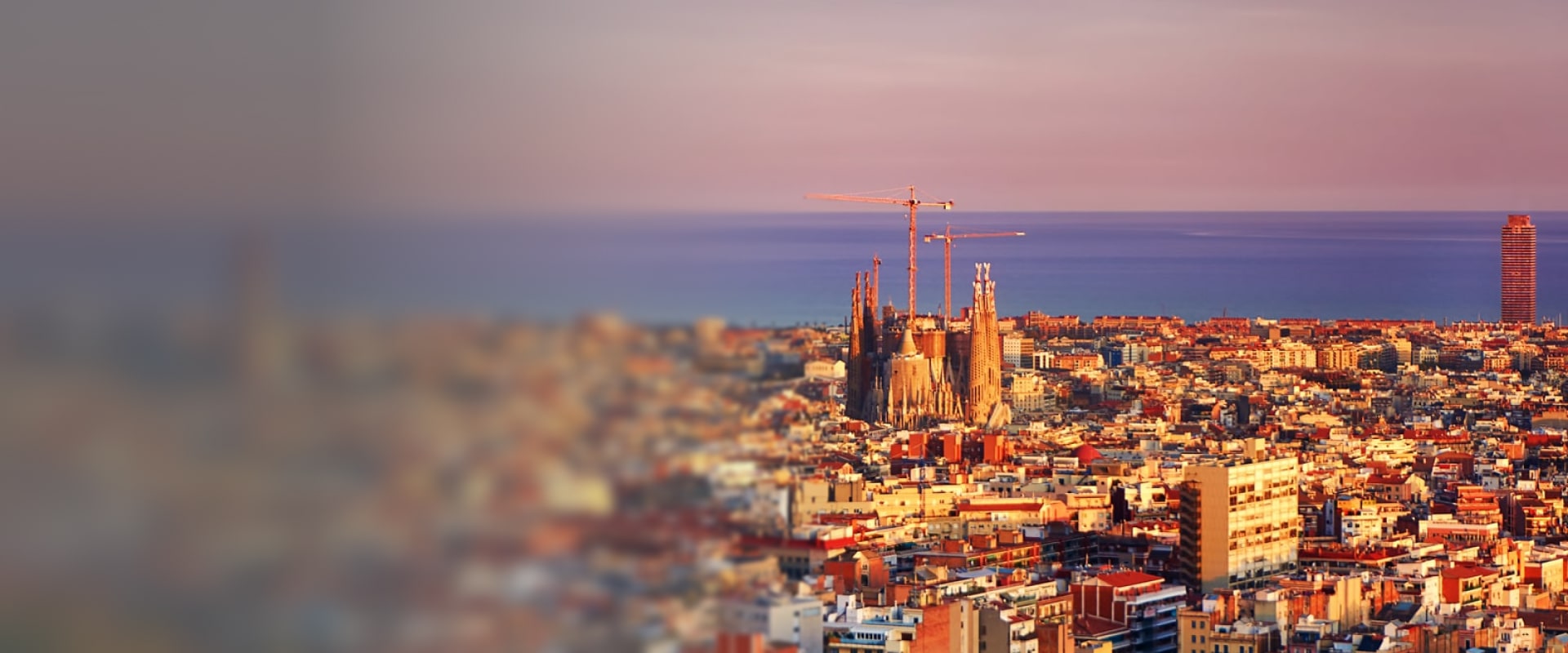 Vue panoramique de Barcelone au coucher du soleil, mettant en évidence la basilique de la Sagrada Família au centre de la ville, avec la mer Méditerranée à l’horizon.