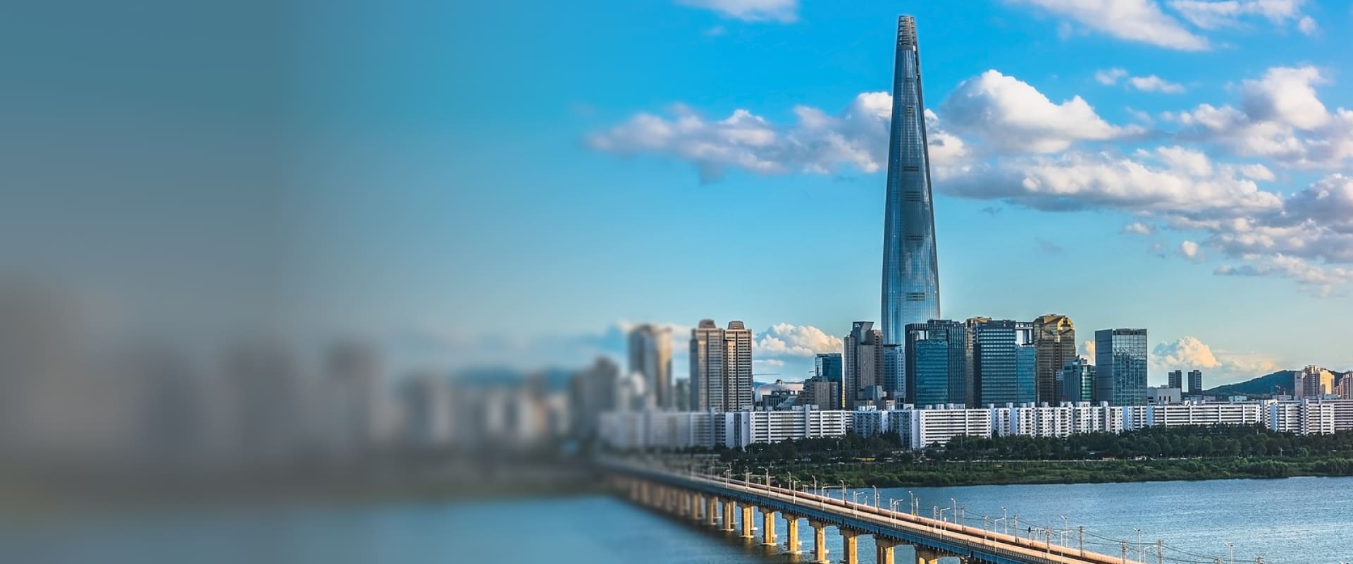 Vue panoramique de Séoul, en Corée du Sud, avec la tour Lotte World Tower dominant le paysage urbain, des immeubles modernes en arrière-plan et un pont traversant la rivière Han sous un ciel bleu.