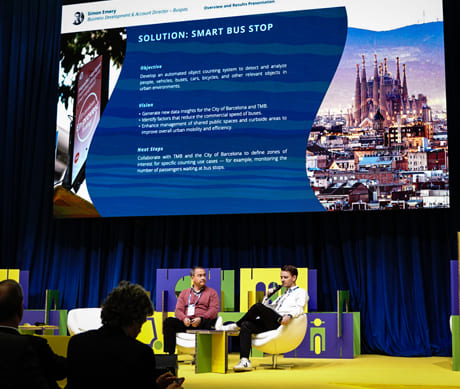 CSpeakers taking part in a discussion on smart mobility at an urban innovation event; a presentation on smart bus stops is displayed on the screen.